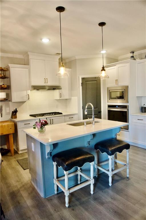 kitchen with appliances with stainless steel finishes, a breakfast bar, decorative light fixtures, white cabinetry, and a center island with sink