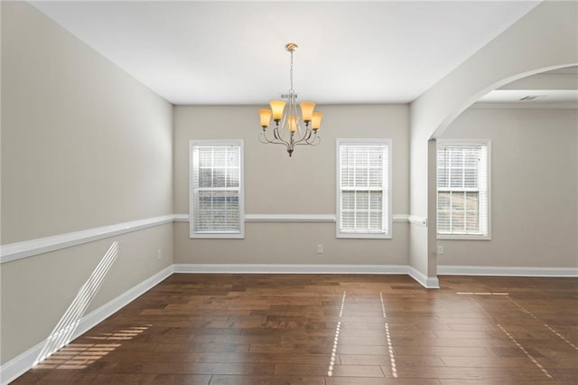 unfurnished room featuring an inviting chandelier, dark hardwood / wood-style flooring, and a wealth of natural light