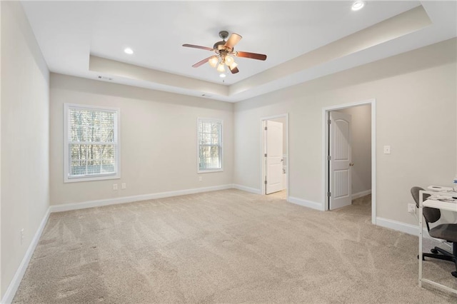 interior space with light carpet, ceiling fan, and a tray ceiling