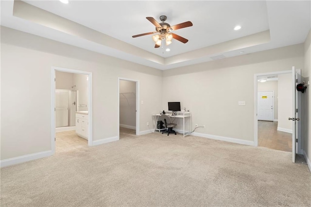 unfurnished office featuring light colored carpet, ceiling fan, and a tray ceiling