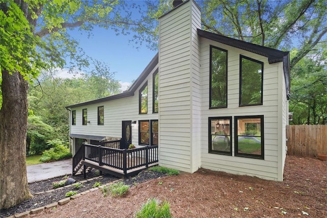 back of house featuring a chimney, a wooden deck, fence, and an attached garage
