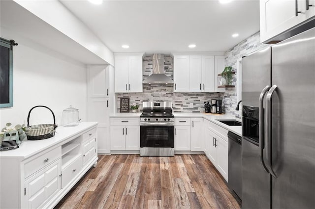 kitchen featuring stainless steel appliances, wall chimney exhaust hood, a sink, decorative backsplash, and white cabinetry