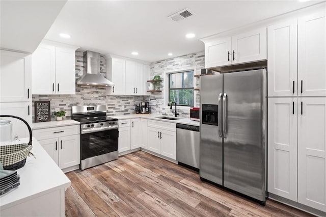 kitchen featuring appliances with stainless steel finishes, wall chimney exhaust hood, a sink, light countertops, and recessed lighting
