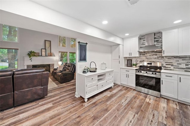 kitchen featuring wall chimney range hood, stainless steel electric range, light countertops, light wood-style flooring, and backsplash