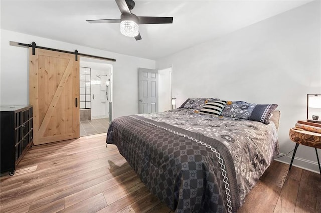 bedroom featuring a barn door, hardwood / wood-style floors, ceiling fan, and ensuite bathroom