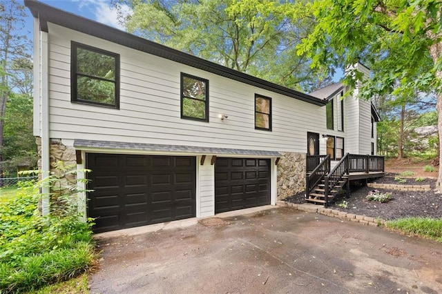 view of front of home featuring a garage, stone siding, concrete driveway, a chimney, and a wooden deck