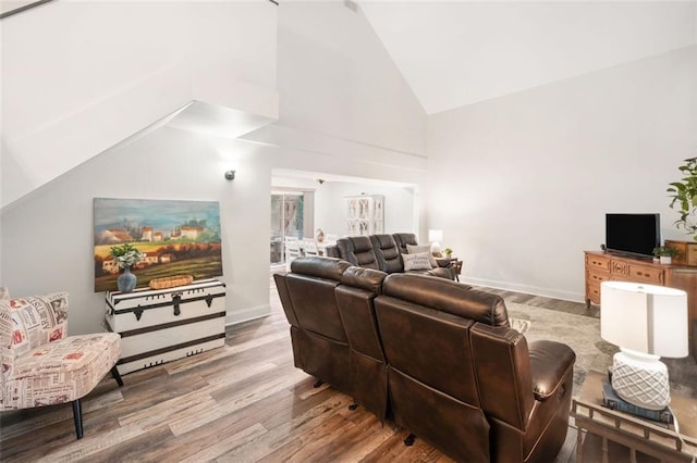 living room featuring wood finished floors, high vaulted ceiling, and baseboards