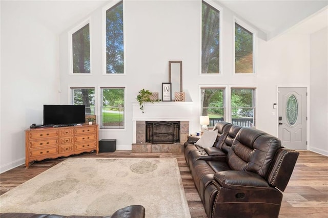 living room featuring high vaulted ceiling, wood finished floors, a fireplace with raised hearth, and baseboards