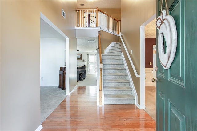 foyer entrance featuring light wood-style floors, visible vents, a high ceiling, and stairway