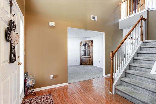 entrance foyer with baseboards, visible vents, stairway, wood finished floors, and a high ceiling