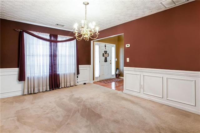 carpeted spare room featuring a textured ceiling, a decorative wall, visible vents, and a notable chandelier