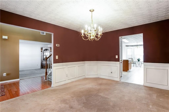 spare room featuring an inviting chandelier, carpet, and a textured ceiling