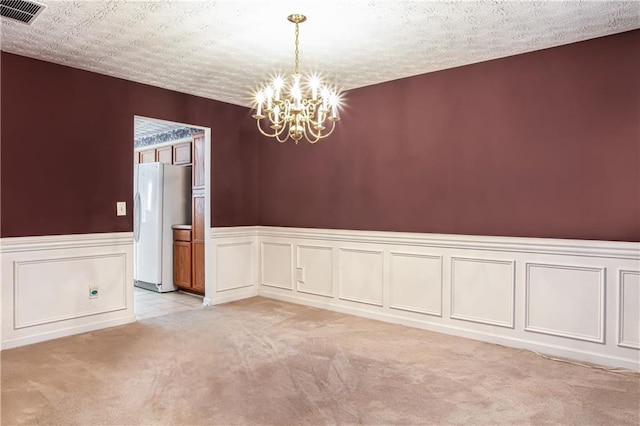 empty room featuring a chandelier, light colored carpet, visible vents, and a textured ceiling