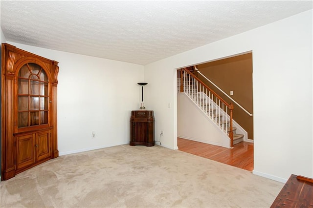 carpeted empty room featuring a textured ceiling, stairway, and baseboards