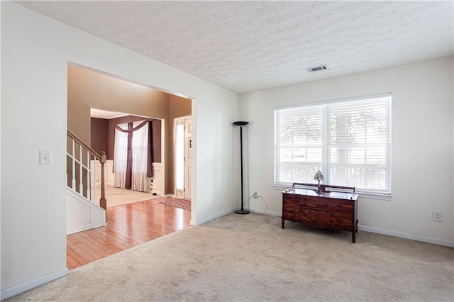 sitting room with stairway, carpet, visible vents, and a textured ceiling