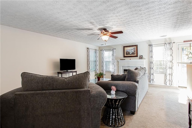 living room with ceiling fan, a textured ceiling, a fireplace, visible vents, and carpet