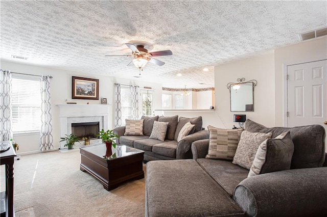 carpeted living room with a high end fireplace, visible vents, ceiling fan, and a textured ceiling