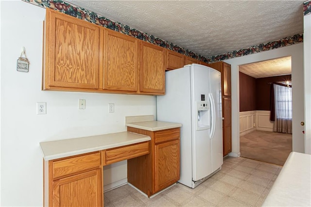 kitchen featuring white refrigerator with ice dispenser, light countertops, wainscoting, built in study area, and light floors