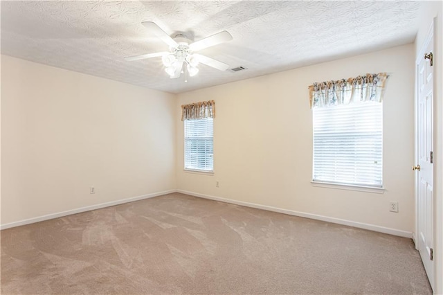 carpeted spare room featuring a ceiling fan, visible vents, a textured ceiling, and baseboards