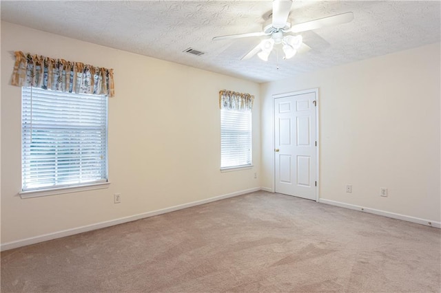 carpeted empty room featuring a textured ceiling, baseboards, visible vents, and a ceiling fan