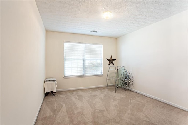 carpeted spare room featuring visible vents, a textured ceiling, and baseboards