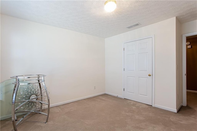 unfurnished bedroom with carpet, visible vents, a textured ceiling, and baseboards