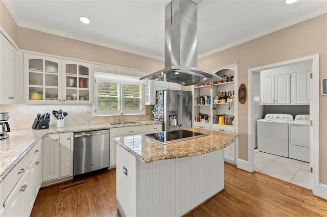 kitchen featuring appliances with stainless steel finishes, washing machine and clothes dryer, a sink, island exhaust hood, and light wood finished floors