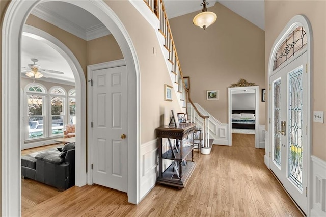 entryway featuring stairway, light wood-type flooring, a ceiling fan, a wainscoted wall, and healthy amount of natural light