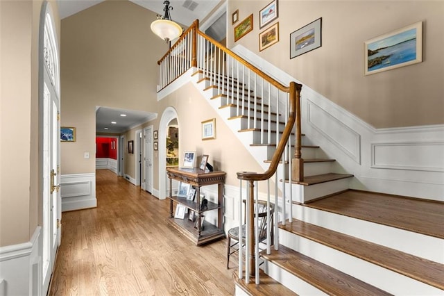 stairs with a decorative wall, a high ceiling, wood finished floors, and a wainscoted wall