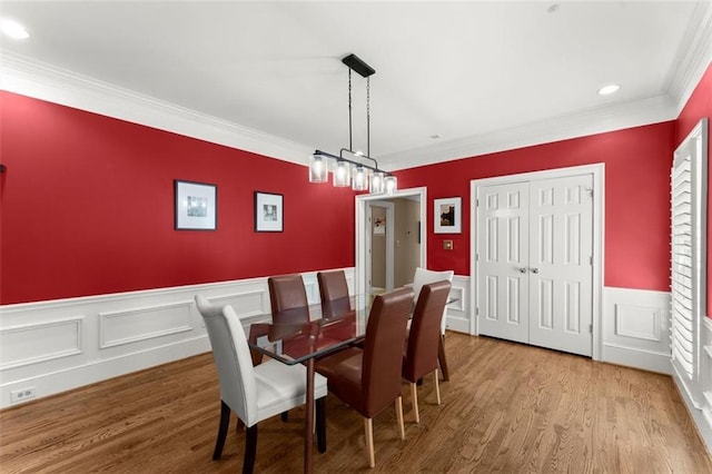 dining space with crown molding, wood finished floors, a wainscoted wall, recessed lighting, and a decorative wall