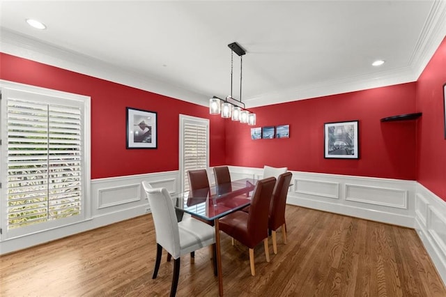 dining space featuring crown molding, wood finished floors, a wainscoted wall, and a decorative wall