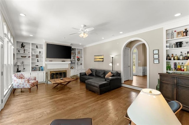 living area with a ceiling fan, wood finished floors, built in features, arched walkways, and a glass covered fireplace