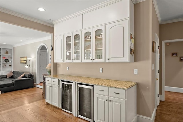 kitchen with wine cooler, arched walkways, white cabinetry, light wood-style floors, and ornamental molding
