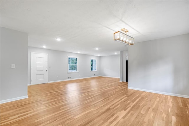 spare room featuring a chandelier, light wood-type flooring, baseboards, and recessed lighting