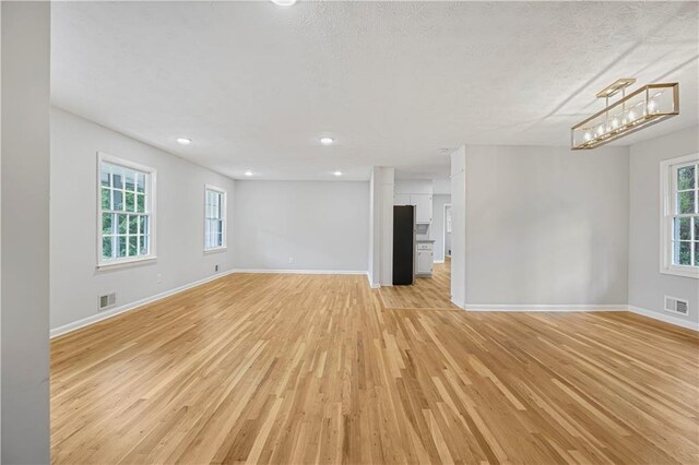 spare room featuring baseboards, visible vents, a textured ceiling, and light wood finished floors