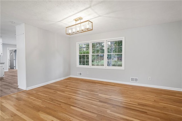 unfurnished room featuring visible vents, a notable chandelier, light wood-style flooring, and a textured ceiling