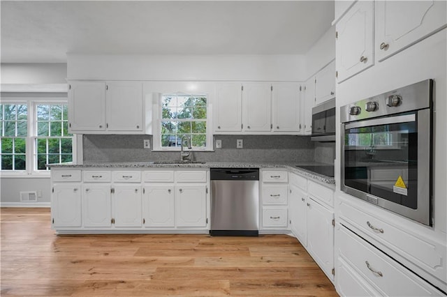 kitchen with stainless steel appliances, a sink, light wood-style flooring, and white cabinets