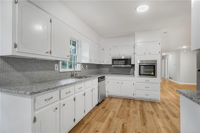 kitchen featuring a sink, light wood-style floors, white cabinets, appliances with stainless steel finishes, and tasteful backsplash