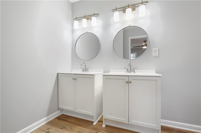 bathroom featuring a sink, baseboards, two vanities, and wood finished floors