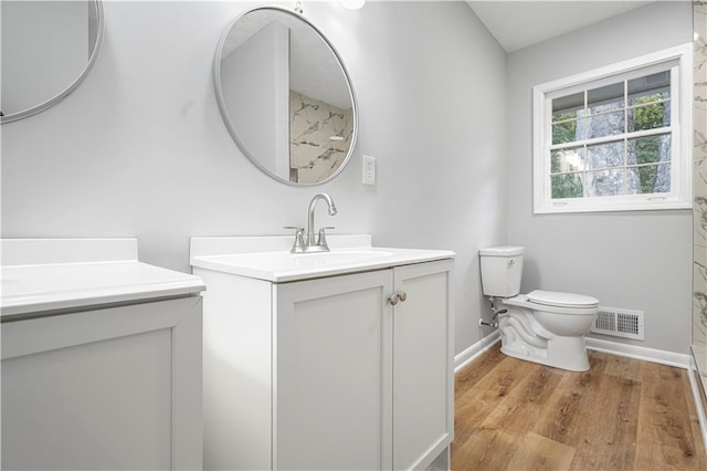 full bath featuring visible vents, toilet, two vanities, wood finished floors, and a sink