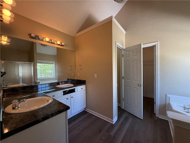 bathroom featuring vaulted ceiling, a shower stall, wood finished floors, two vanities, and baseboards