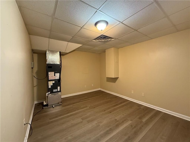 finished below grade area with a drop ceiling, dark wood-style flooring, baseboards, and heating unit