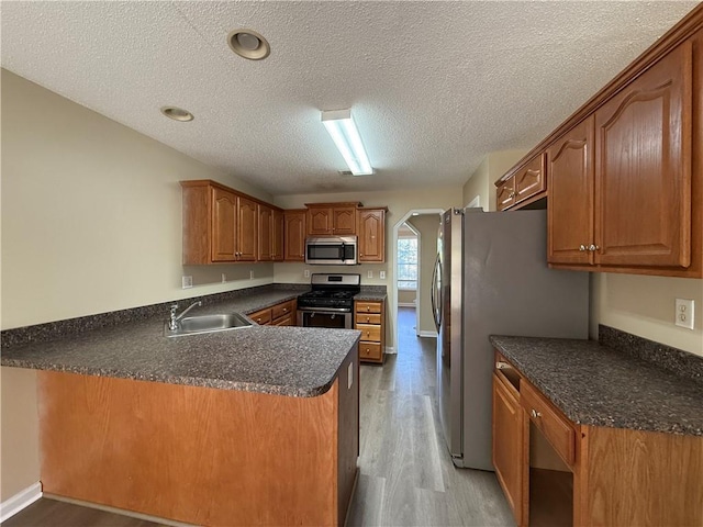 kitchen featuring stainless steel appliances, a sink, light wood-style floors, a peninsula, and a textured ceiling