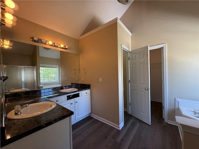 full bath featuring a shower stall, wood finished floors, lofted ceiling, two vanities, and baseboards