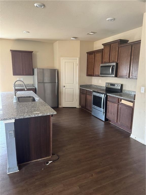 kitchen featuring visible vents, a sink, light stone counters, dark wood-style floors, and stainless steel appliances