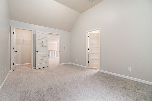 unfurnished bedroom with light carpet, vaulted ceiling, a spacious closet, and a closet