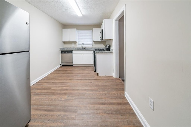 kitchen featuring appliances with stainless steel finishes, light wood-type flooring, a textured ceiling, sink, and white cabinetry