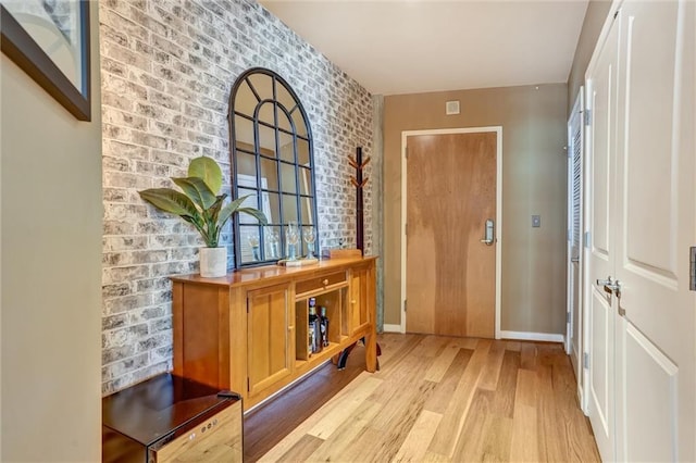 doorway featuring brick wall, wood finished floors, and baseboards