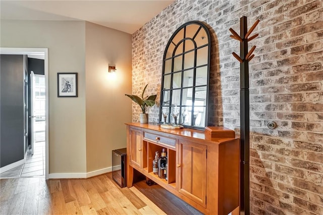 interior space with brick wall, light wood finished floors, and baseboards