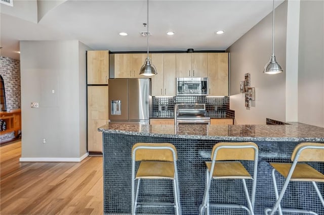 kitchen with light wood-style floors, hanging light fixtures, appliances with stainless steel finishes, dark stone counters, and tasteful backsplash